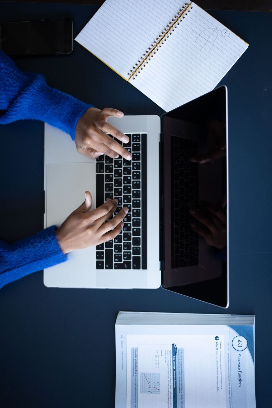 Hands working on a laptop at a desk, seen from above.