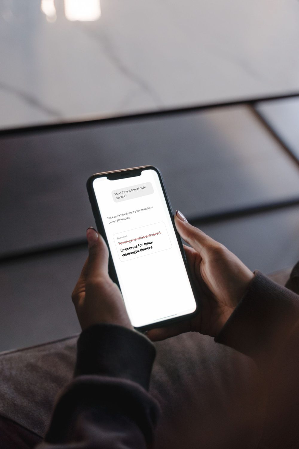 A hand holding a phone showing an ad being rewritten by ChatGPT.